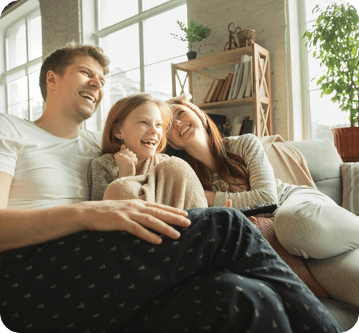 A photo of a family of three smiling whilst sitting on a sofa